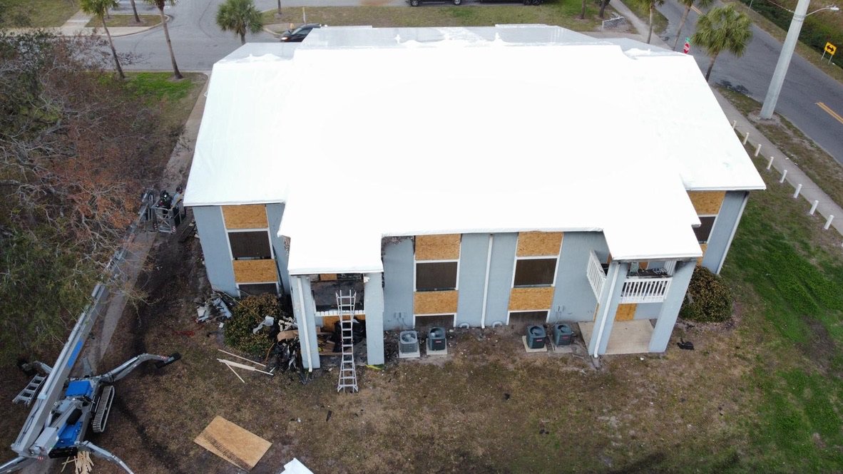 The same apartment building sealed watertight under a white Elastowrap roof after the fire