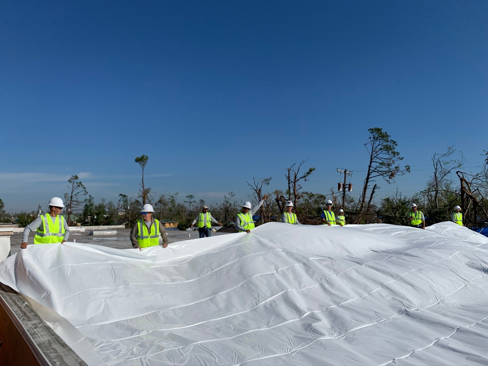 Titanium Tarps crew in hi-vis pulling a white Elastowrap membrane across a roof