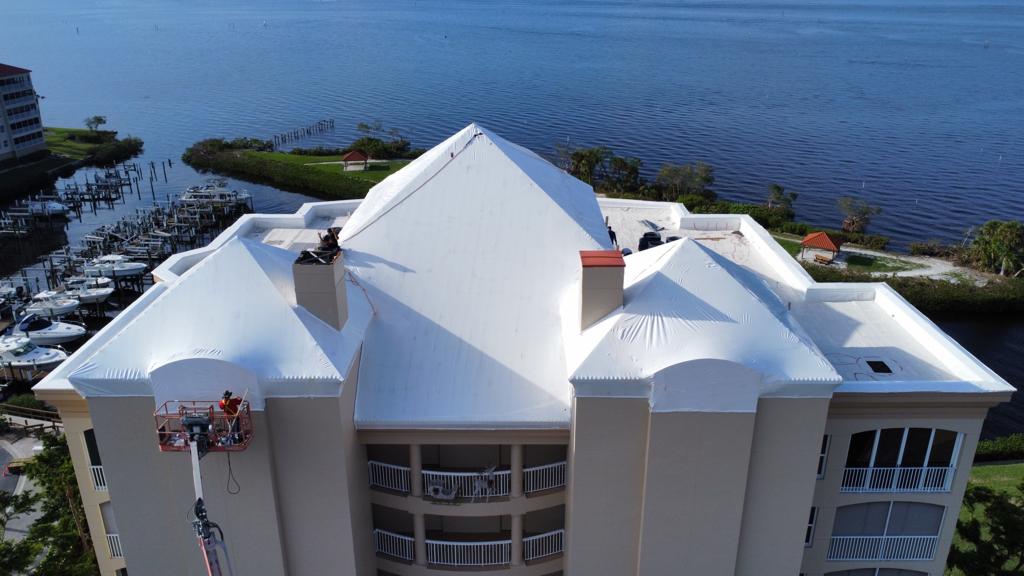 Crew sealing a waterfront commercial building roof under white Titanium Tarps Elastowrap, boom lift in place