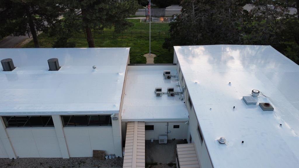Twin government facility roofs sealed white under Titanium Tarps Elastowrap, flagpole between them